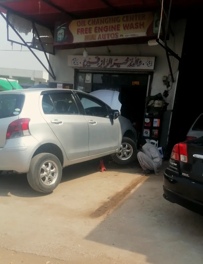 A Toyota Vitz raised on a jack while a mechanic works underneath, beside the oil changing center sign